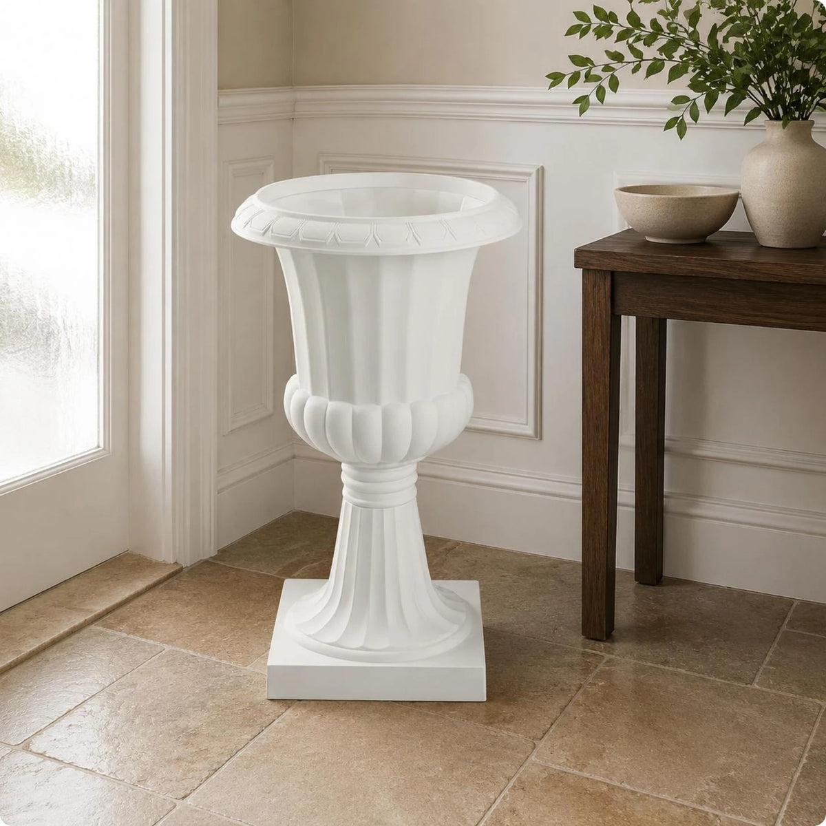 Maceta blanca acanalada con pedestal alto junto a una ventana.