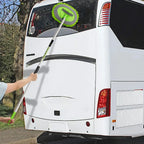 Persona usando el cepillo verde de mango largo para lavar la ventana trasera de un autobús