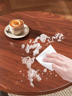 Mano limpiando líquido derramado sobre la cubierta café de la mesa auxiliar