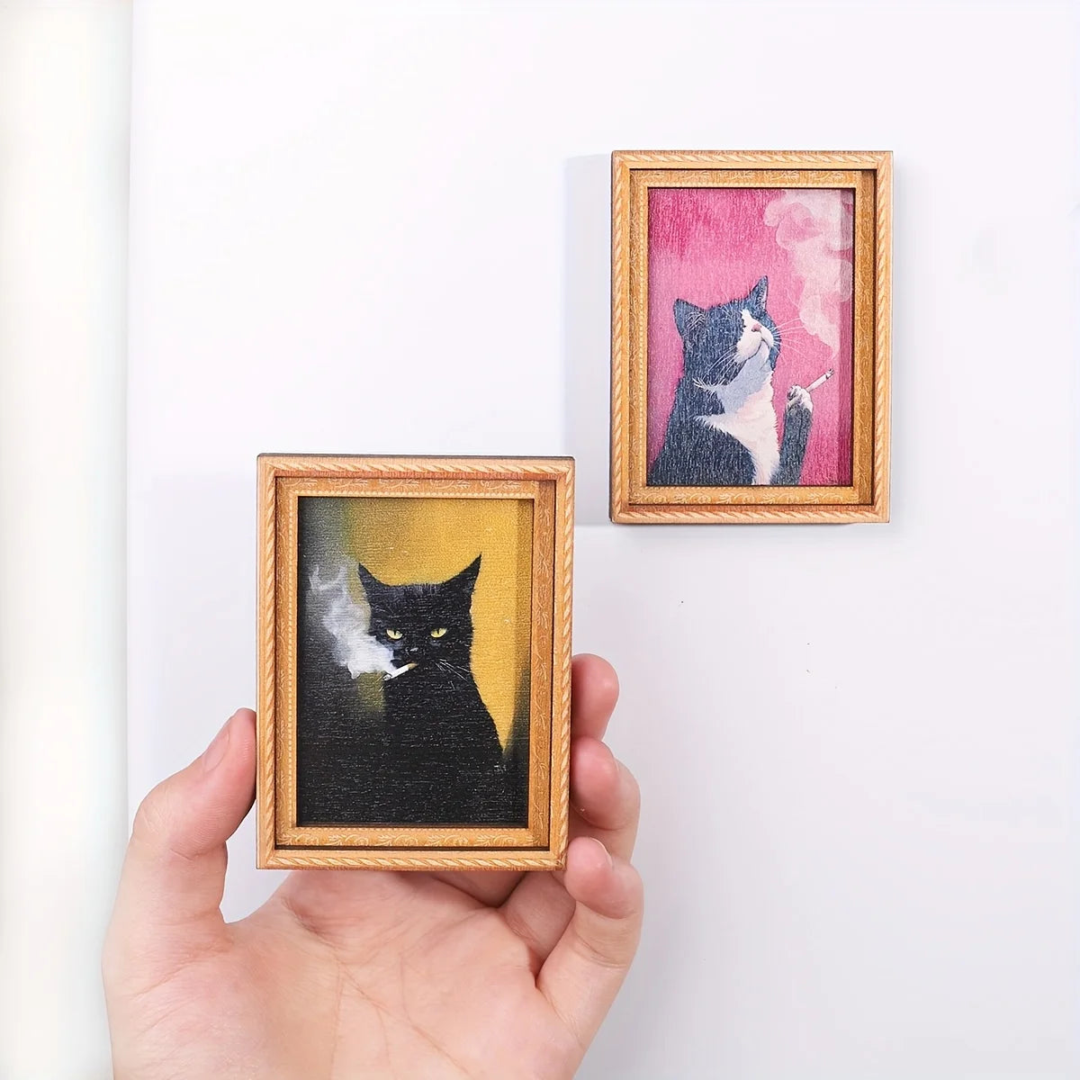 Mano sosteniendo un imán con retrato de gato negro sobre fondo ocre.
