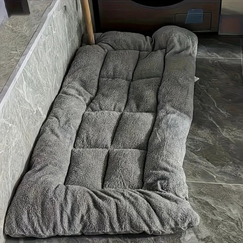 Cama rectangular gris con bordes acolchados y costuras en el centro.