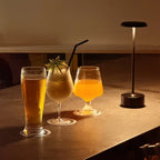 Lámpara negra junto a dos bebidas, iluminando una mesa.