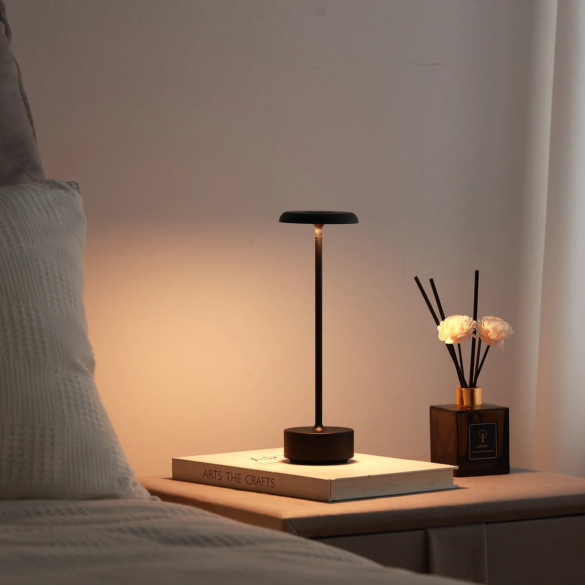 Lámpara de mesa negra encendida junto a una cama.