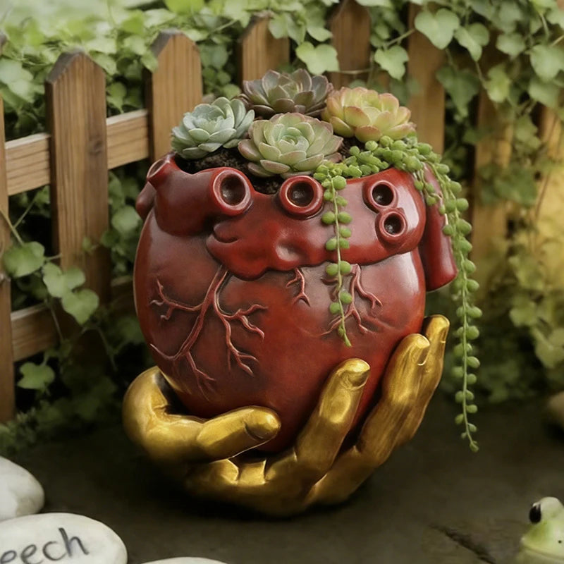 Maceta decorativa de corazón rojo con mano dorada y follaje colgante.