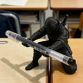 Portapluma negro de ninja sosteniendo una pluma transparente sobre escritorio