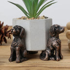 Dos soportes con forma de perro junto a una maceta gris.