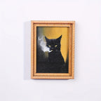 Imán con marco dorado y retrato de gato negro fumando sobre fondo ocre.