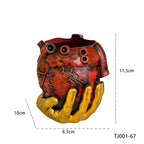 Maceta de corazón rojo y mano dorada con medidas de 11.5 por 10 por 8.5 cm.