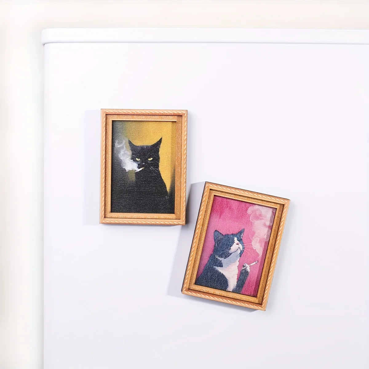 Dos imanes de gatos con marco dorado colocados en un refrigerador.