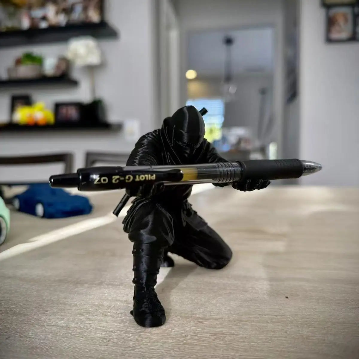 Figura negra de ninja sujetando una pluma, vista frontal sobre escritorio