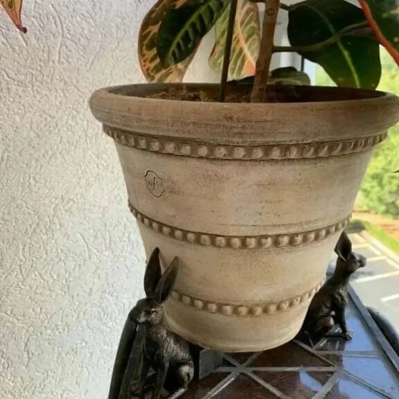Soportes de animales bajo una maceta decorativa en una mesa exterior.