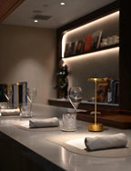 Lámpara de mesa dorada iluminando una mesa de restaurante.