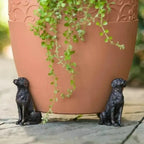 Soportes para maceta en forma de perro, colocados bajo una maceta de barro.