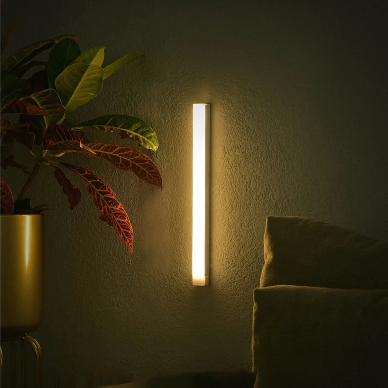 Barra LED encendida con luz cálida sobre una pared junto a una planta