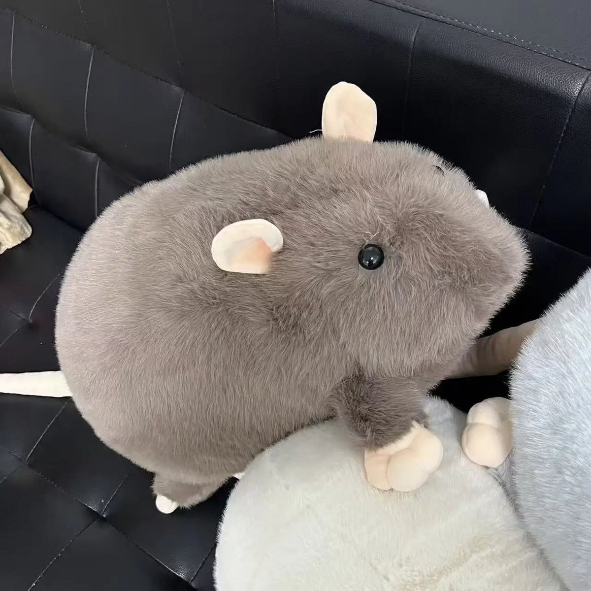 Ratón de peluche café con orejas claras sobre un sillón negro