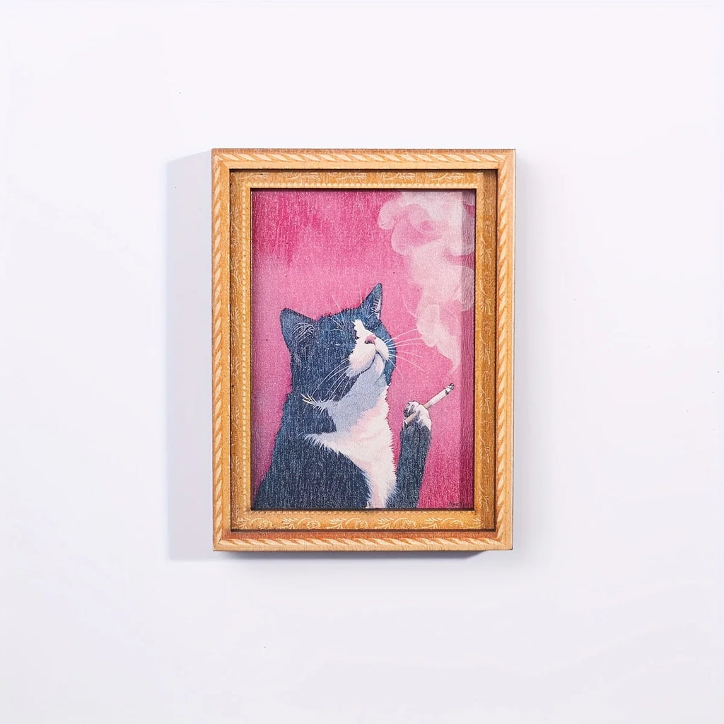 Imán con marco dorado y gato blanco y negro fumando sobre fondo rosa.