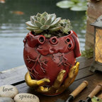 Maceta de corazón con mano dorada junto al agua.