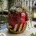 Maceta de corazón rojo y mano dorada en un jardín, con suculentas.