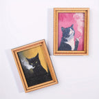 Dos imanes con marco dorado y retratos de gatos fumando, sobre fondos rosa y ocre.